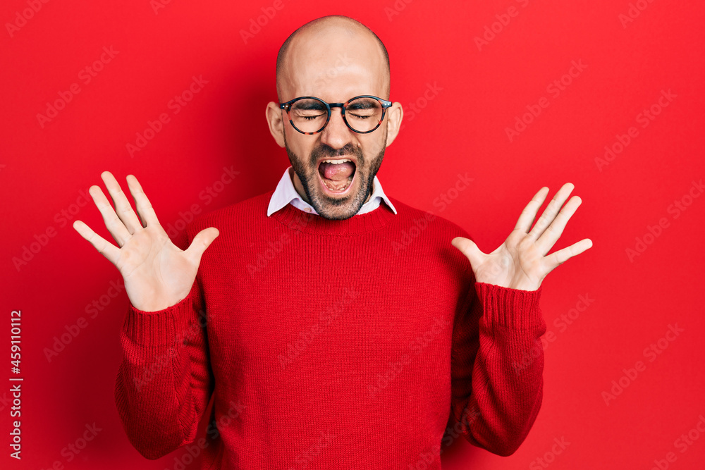 Young bald man wearing casual clothes and glasses celebrating mad and crazy for success with arms raised and closed eyes screaming excited. winner concept Young bald man wearing casual clothes and glasses celebrating mad and crazy for success with arms raised and closed eyes screaming excited. winner concept