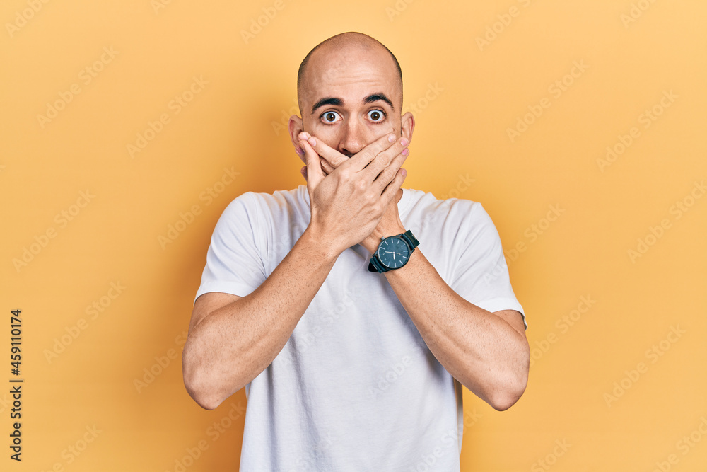 Young bald man wearing casual white t shirt shocked covering mouth with hands for mistake. secret concept. Young bald man wearing casual white t shirt shocked covering mouth with hands for mistake. secret concept.