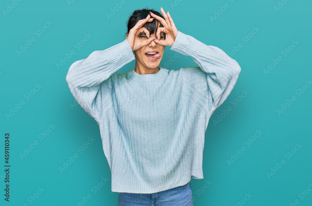 Fototapeta premium Young hispanic woman wearing casual clothes doing ok gesture like binoculars sticking tongue out, eyes looking through fingers. crazy expression.