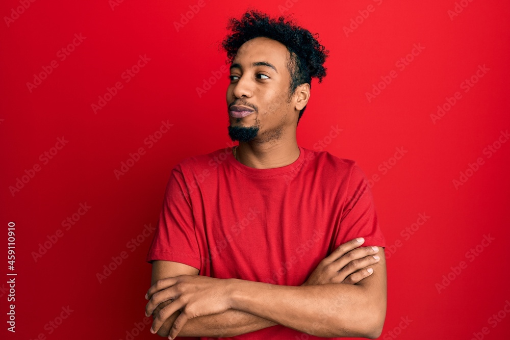Young african american man with beard wearing casual red t shirt smiling looking to the side and staring away thinking. Young african american man with beard wearing casual red t shirt smiling looking to the side and staring away thinking.