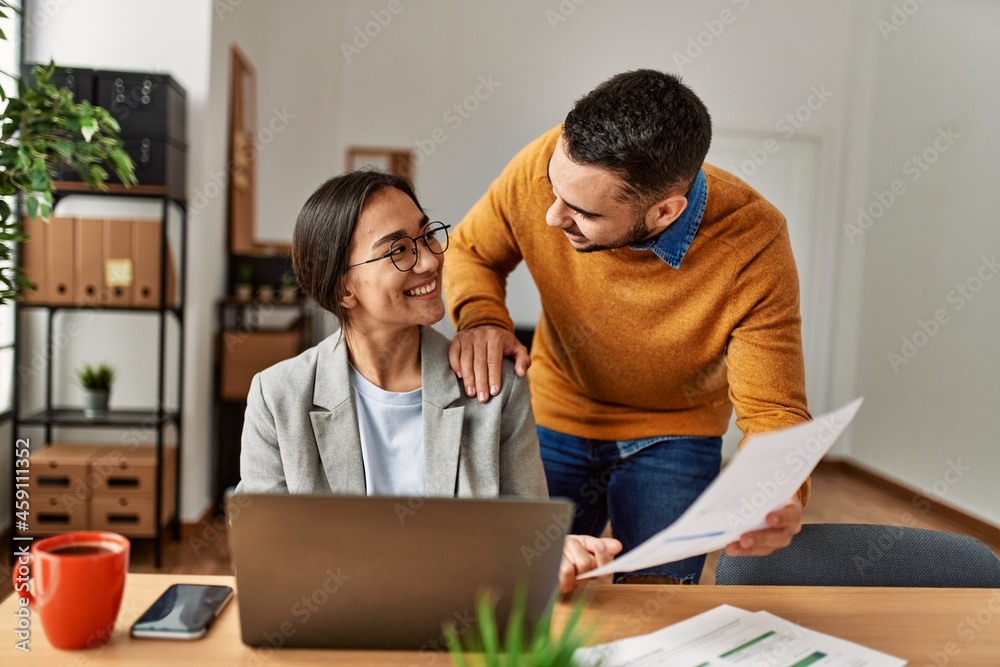 Two business workers smiling happy working sitting on desk at the office. Two business workers smiling happy working sitting on desk at the office.