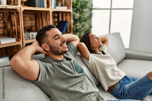 Young latin couple resting with head on hands sitting on the sofa at home.