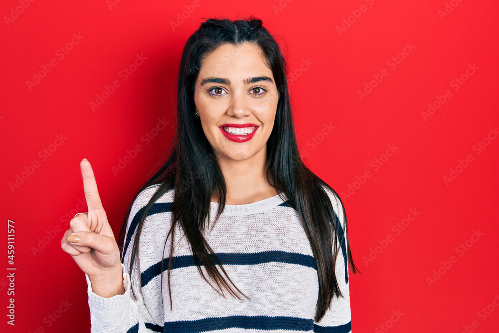Young hispanic girl wearing casual clothes showing and pointing up with finger number one while smiling confident and happy. Young hispanic girl wearing casual clothes showing and pointing up with finger number one while smiling confident and happy.