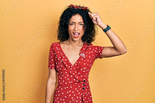 Young latin girl wearing summer dress angry and mad raising fist frustrated and furious while shouting with anger. rage and aggressive concept.