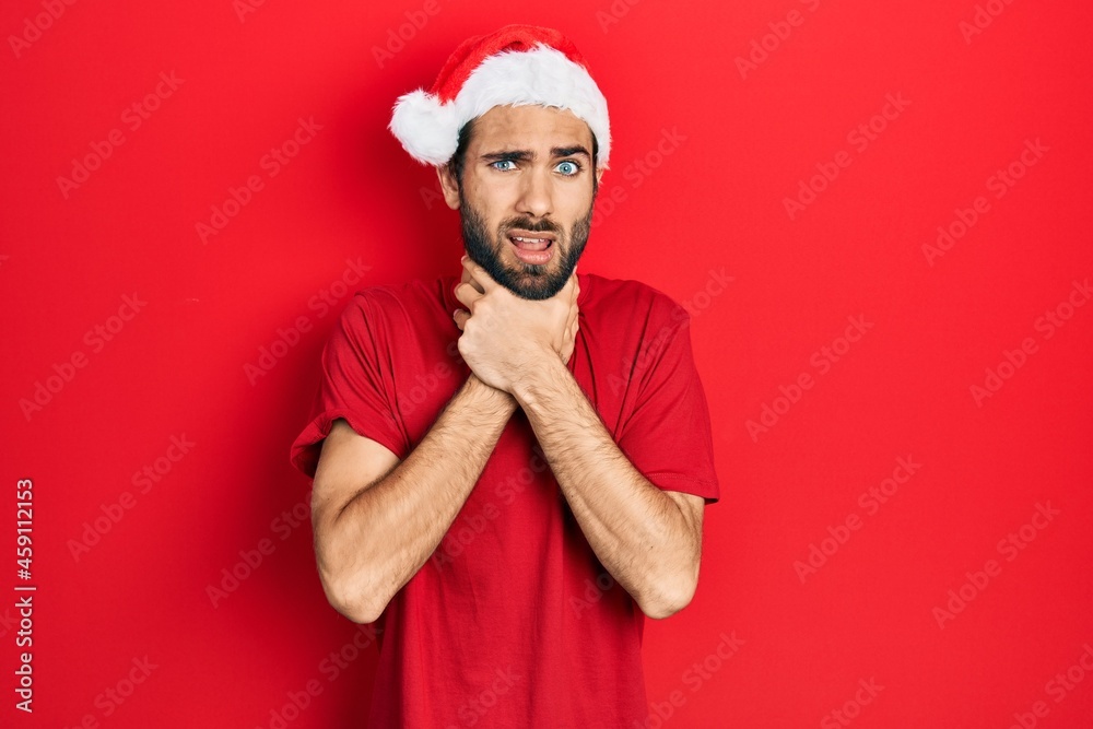 Young hispanic man wearing christmas hat shouting and suffocate because painful strangle. health problem. asphyxiate and suicide concept. Young hispanic man wearing christmas hat shouting and suffocate because painful strangle. health problem. asphyxiate and suicide concept.