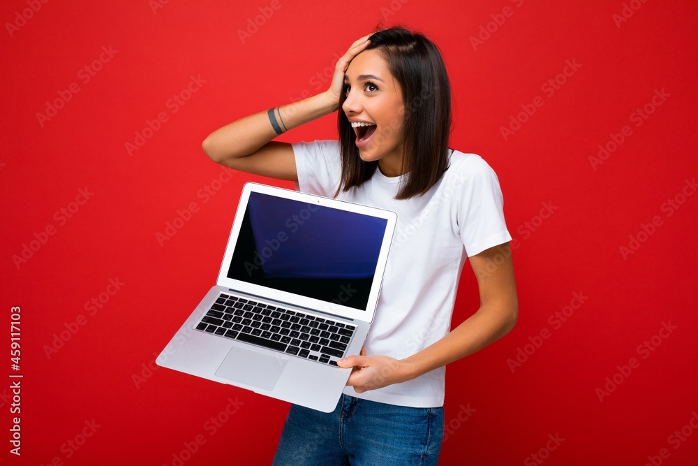 Shocked astonished Beautiful happy overjoyed young female person with short dark brunet haircut holding computer laptop looking to the side wearing holding head with emotions white t-shirt and jeans Shocked astonished Beautiful happy overjoyed young female person with short dark brunet haircut holding computer laptop looking to the side wearing holding head with emotions white t-shirt and jeans