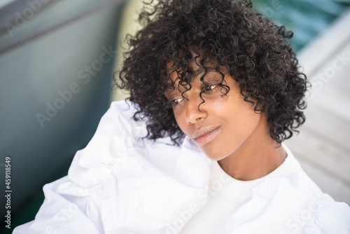 Close up of thoughtful african american woman with curly hair looking away on boat. Beautiful black woman in white dress deep in thoughts. Female tourist daydreaming outdoors