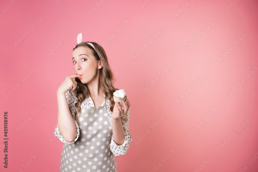 young charming female pastry chef tastes a muffin with cream. A cook in a polka-dot apron. young charming female pastry chef tastes a muffin with cream. A cook in a polka-dot apron.