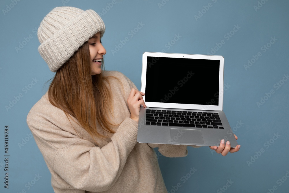 photo shot of beautiful charming fascinating pretty smiling happy young dark blond woman in winter warm knitted beige hat holding computer laptop looking at netbook empty free copy space monitor and photo shot of beautiful charming fascinating pretty smiling happy young dark blond woman in winter warm knitted beige hat holding computer laptop looking at netbook empty free copy space monitor and