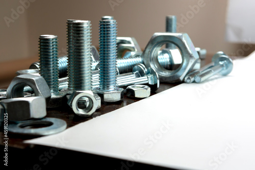 Several metal bolts and nuts on a wooden table next to a white background
