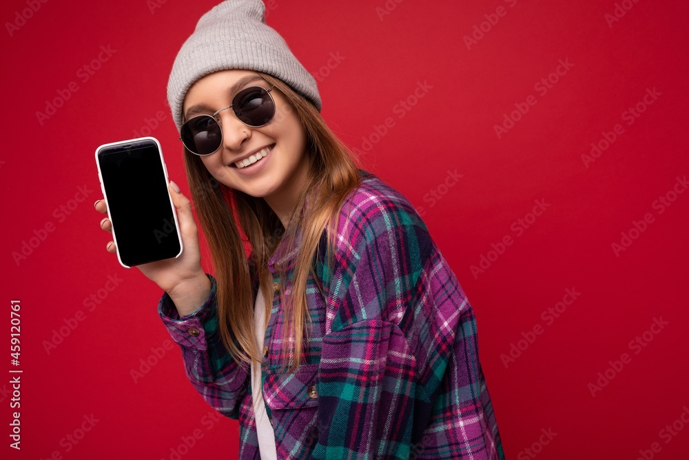 Photo of beautiful smiling young woman good looking wearing casual stylish outfit standing isolated on background with copy space holding smartphone showing phone in hand with empty screen display for Photo of beautiful smiling young woman good looking wearing casual stylish outfit standing isolated on background with copy space holding smartphone showing phone in hand with empty screen display for