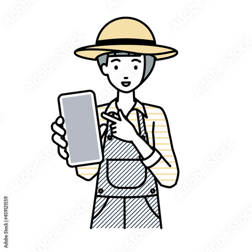 立ってスマートフォンを指差してこちらに向けて見せている農家の女性
