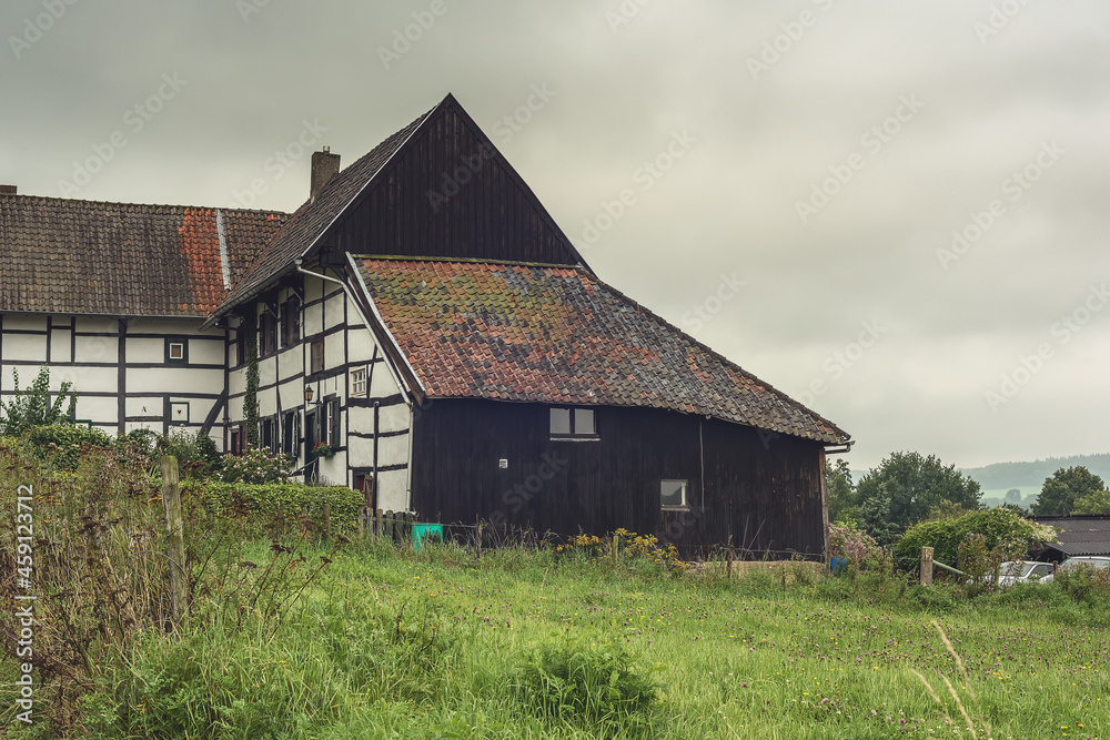 Obraz premium Old half-timbered farmhouse with wooden shed in a lush hilly landscape.