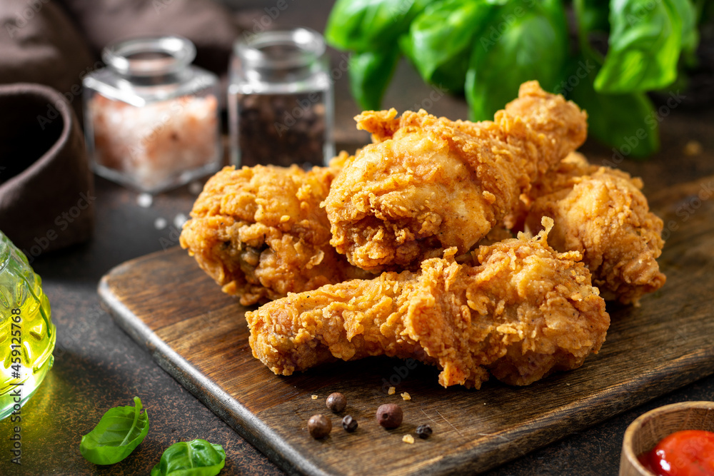 Fried crispy chicken legs in breadcrumbs on a wooden serving board on a dark background. Fast food from the drumstick close-up