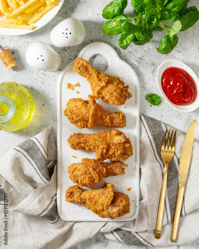 Fried crispy chicken legs in breadcrumbs on a white ceramic serving board on a light culinary background. Fast food from the drumstick top view