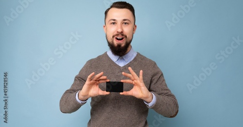 Panoramic photo of Handsome smiling brunette bearded guy wearing grey sweater and blue shirt isolated on background wall holding credit card looking at camera photo