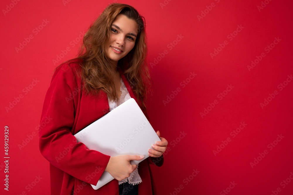 Photo of beautiful young girl holding computer laptop looking at camera isolated over colourful background Photo of beautiful young girl holding computer laptop looking at camera isolated over colourful background