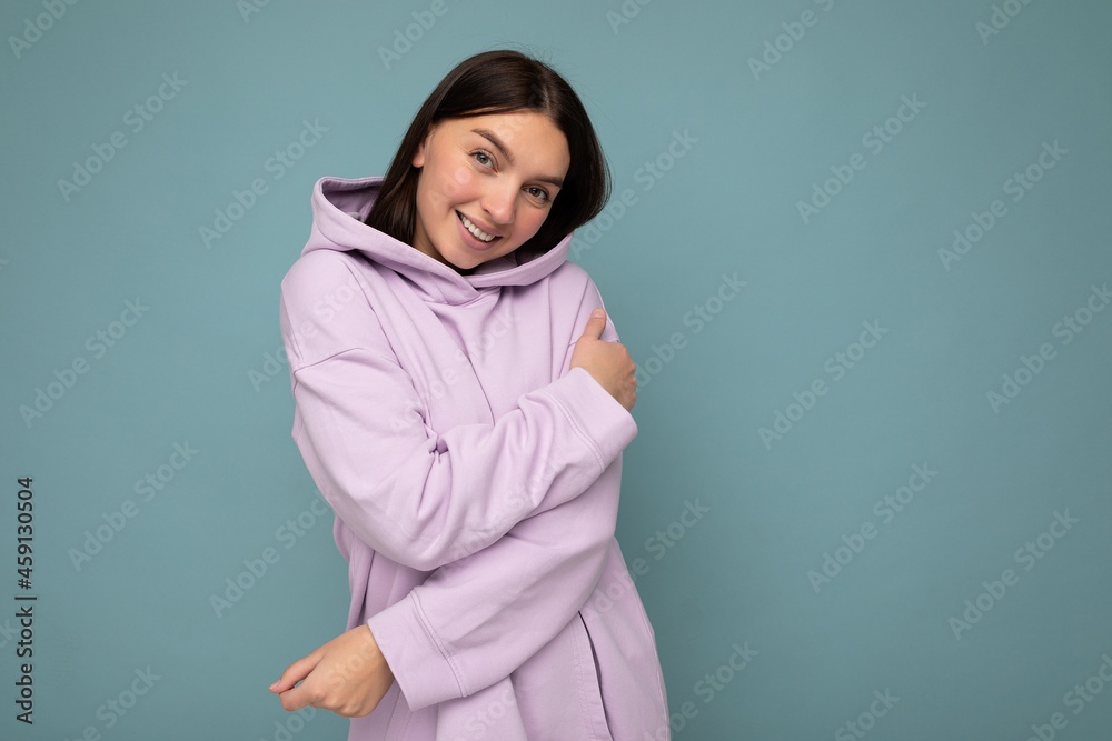 Smiling cute young beautiful brunette woman with sincere emotions isolated on background wall with copy space wearing casual stylish purple hoodie. Positive concept Smiling cute young beautiful brunette woman with sincere emotions isolated on background wall with copy space wearing casual stylish purple hoodie. Positive concept
