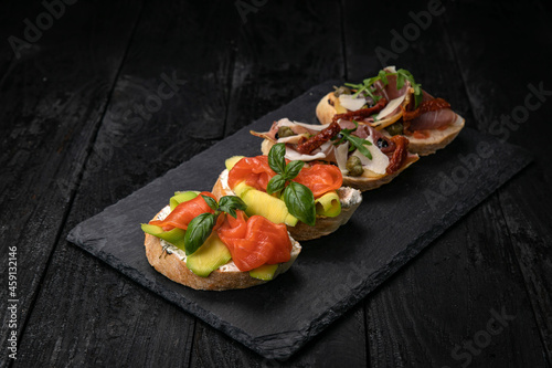 Bruschetta with salmon and meat on a dark wooden table
