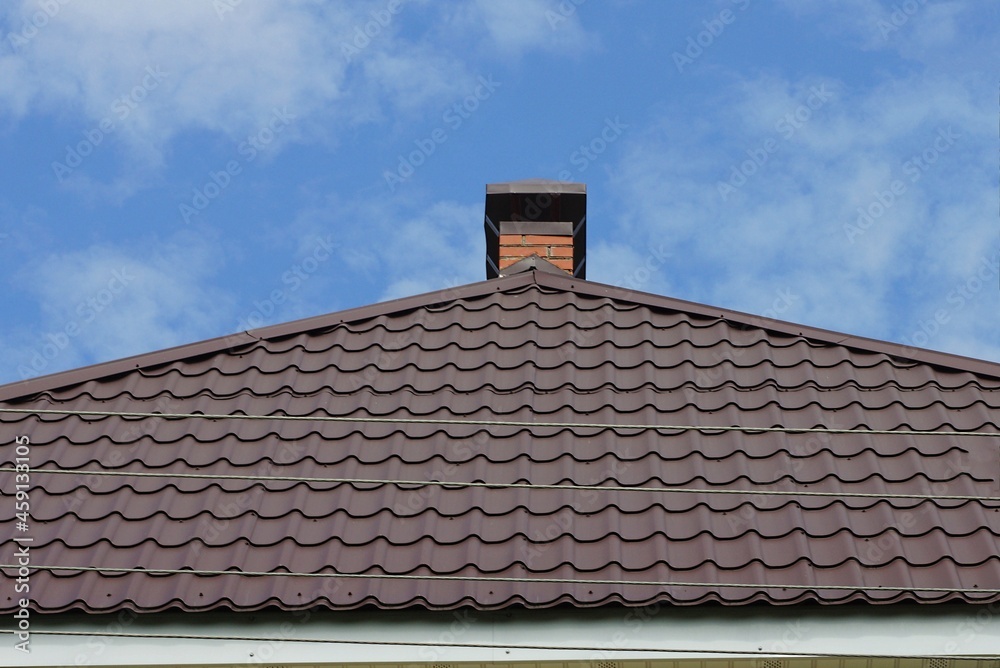 one brick metal chimney on the brown tiled roof of a private house against the blue sky