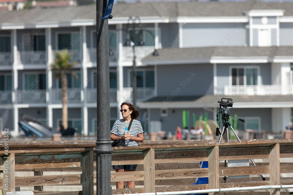A Woman Video Journalist Documenting and Videoing Pismo Beach, California, with a Video Camera from the Pier