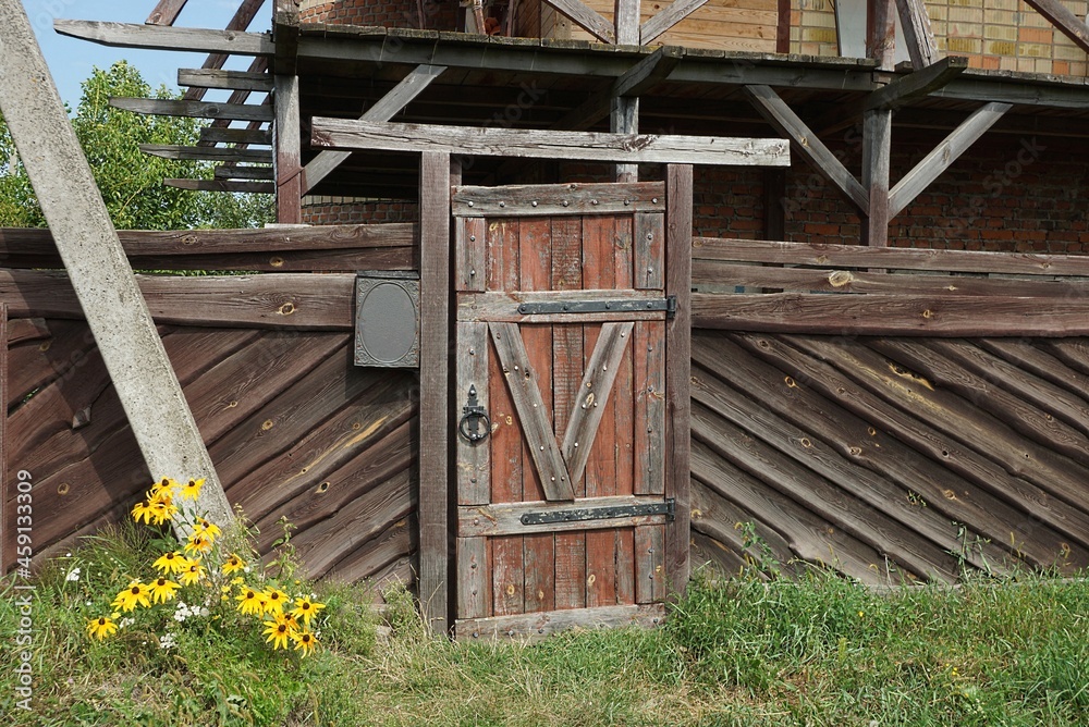 Naklejka premium one closed old wooden door and part of a brown fence wall on a rural street