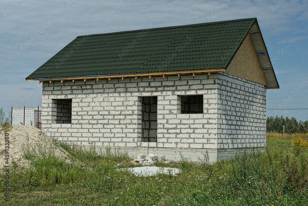 unfinished white private brick house with a green tiled roof in the grass against the sky unfinished white private brick house with a green tiled roof in the grass against the sky
