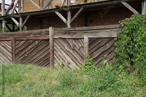 brown gray wall of a rural fence made of wooden boards in green grass on the street