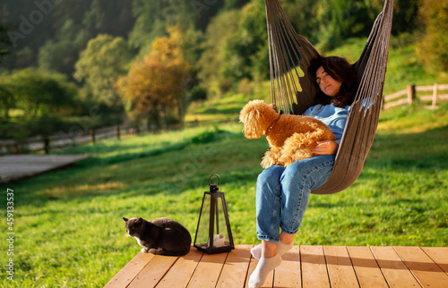 Woman with dog and cat resting on the hanging
chair on the terrace mountain chalet. On the mountain
background.