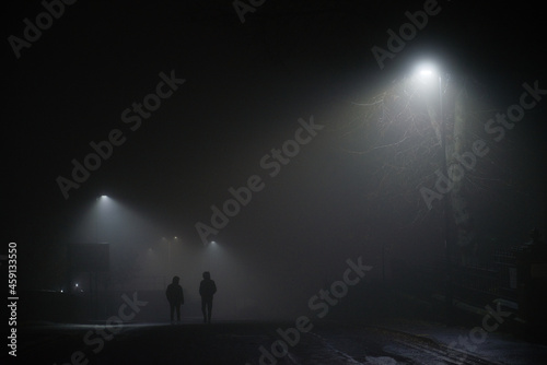 Urban winters scene of two men walking under street lights, foggy