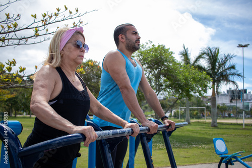 blonde white lady doing physical activity on gym equipment in the park with her friend.