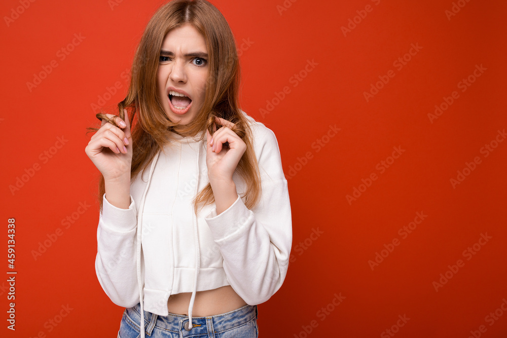 Fototapeta premium Young emotional dissatisfied beautiful dark blonde woman with sincere emotions isolated on background wall with copy space wearing casual hoodie. Feelings concept