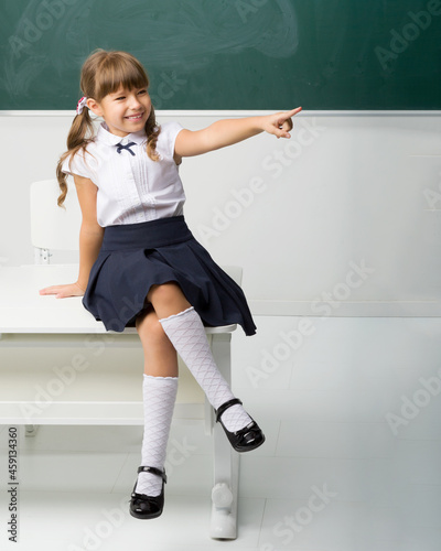 Happy school girl sitting on desk in classroom