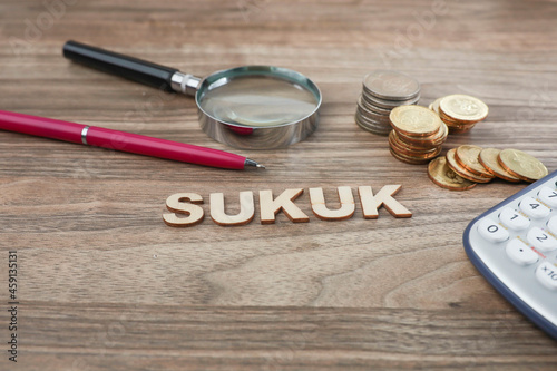 SUKUK as an alternative financing source concept. Pen, magnifying glass, and coins stacked on the wooden table 