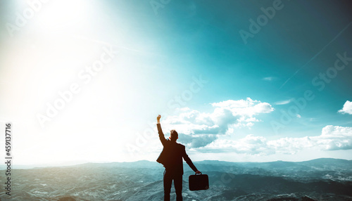 Silhouette of successful businessman keeping hands up hiking on the top of mountain - Celebrating success, winner and leader concept	
