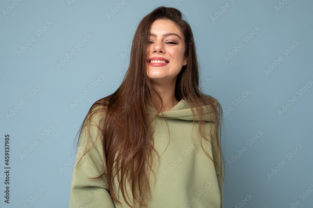 Young beautiful woman looking at camera. Trendy girl in casual hipster hoodie clothes. Positive female shows facial emotions. Funny model isolated on blue background with free space for text Young beautiful woman looking at camera. Trendy girl in casual hipster hoodie clothes. Positive female shows facial emotions. Funny model isolated on blue background with free space for text