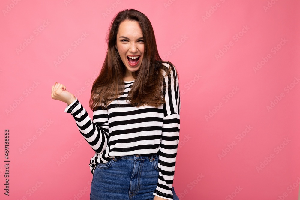 Portrait of young emotional positive happy nice cute brunette woman with sincere emotions in casual striped pullover isolated on pink background with free space and celebrating winning shouting yes Portrait of young emotional positive happy nice cute brunette woman with sincere emotions in casual striped pullover isolated on pink background with free space and celebrating winning shouting yes