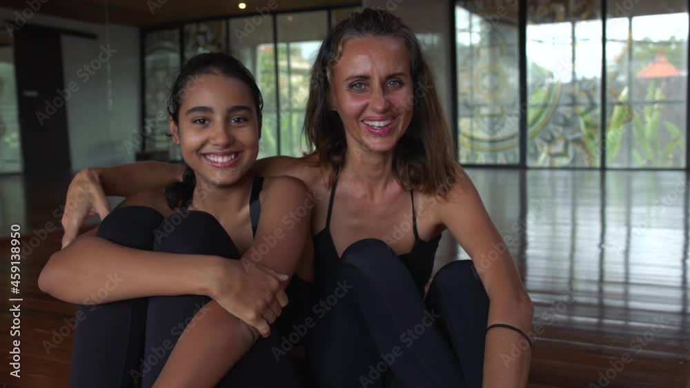 Portrait of a happy middle-aged mother coach and teen daughter wearing sports outfit is looking into the camera in the dance studio Portrait of a happy middle-aged mother coach and teen daughter wearing sports outfit is looking into the camera in the dance studio