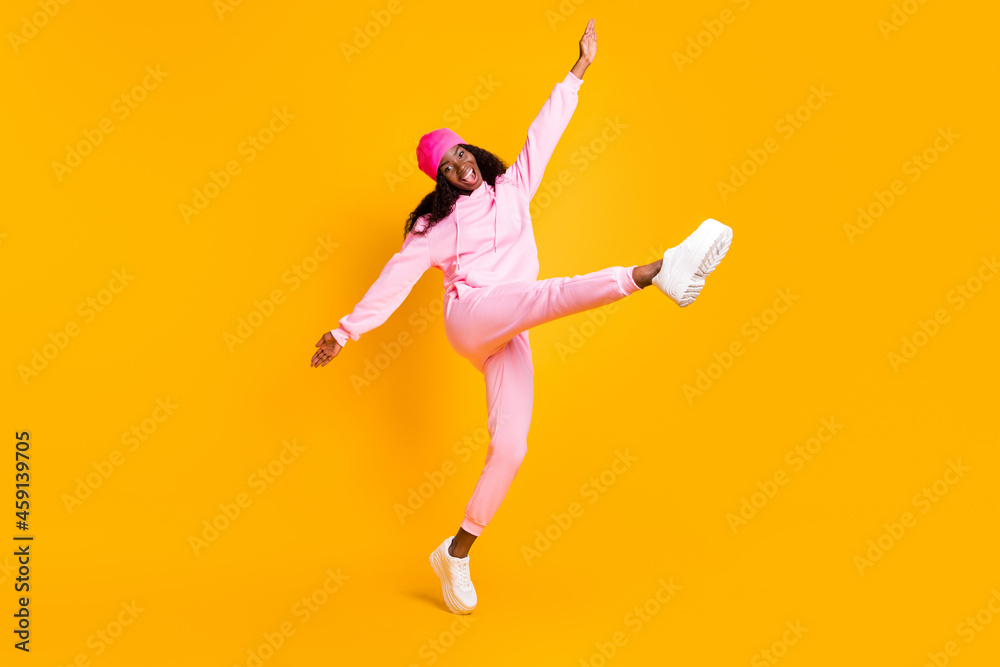 Full length photo portrait of dark skin girl kicking standing on one leg isolated on vivid yellow colored background Full length photo portrait of dark skin girl kicking standing on one leg isolated on vivid yellow colored background