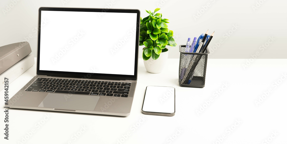 A blank white screen laptop on white table in the office. Blank white screen smartphone. Working concept using technology. Copy space on right for design or text, Closeup, Gray, and blurred background