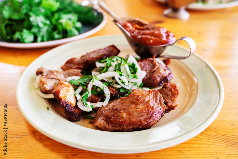 Pork shashlik on a white plate decorated with herbs. Grilled meat on charcoal with tomato sauce lies on a wooden table. Close-up. Selective focus