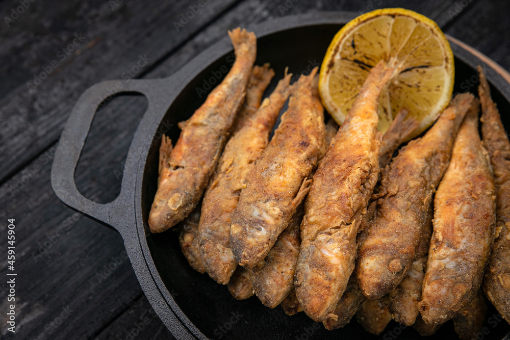 Fried fish on a black cast iron skillet on a dark wooden table
