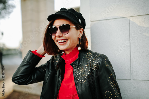 Close-up portrait of cheerful white woman in glasses touching her hat on blur background. Photo of fashionable girl with short brown hair smiling to camera.