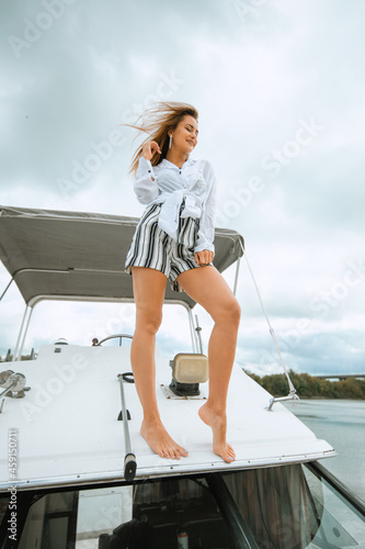 Woman dancing standing on the nose of the yacht at a sunny summer day, breeze developing hair. Having fun together and enjoying the sun while sailing in the sea. Traveling and yachting concept. © Air_Lady