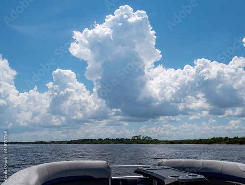 White puffy clouds with blue sky background.  Green shore line with red buoy. pontoon boat traveling on the intercoastal waterway.