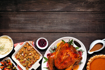 Traditional Thanksgiving turkey dinner. Top view bottom border on a dark rustic wood background with copy space. Turkey, mashed potatoes, dressing, pumpkin pie and sides.