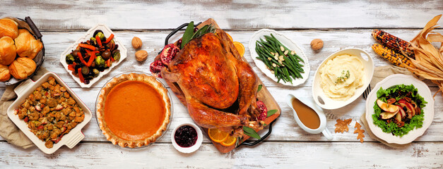 Traditional Thanksgiving turkey dinner. Above view table scene on a rustic white wood banner background. Turkey, mashed potatoes, stuffing, pumpkin pie and sides.