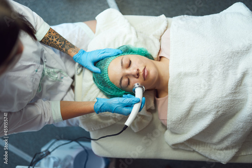 Cosmetologist performs phonophoresis procedure for the skin of young woman in beauty salon.