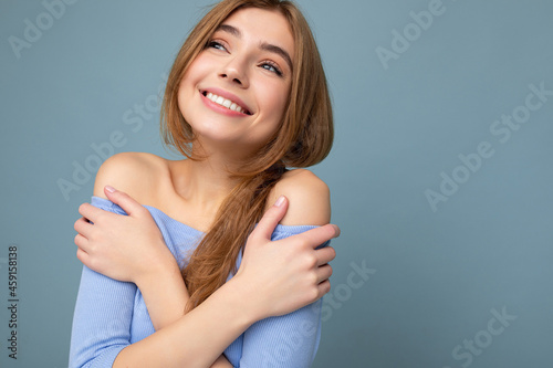 Young attractive smiling dark blonde woman with sincere emotions isolated on background wall with copy space wearing casual blue crop top. Positive concept