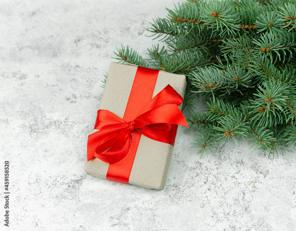 Gift box with a red bow and fir branches on a light background. Christmas composition Gift box with a red bow and fir branches on a light background. Christmas composition